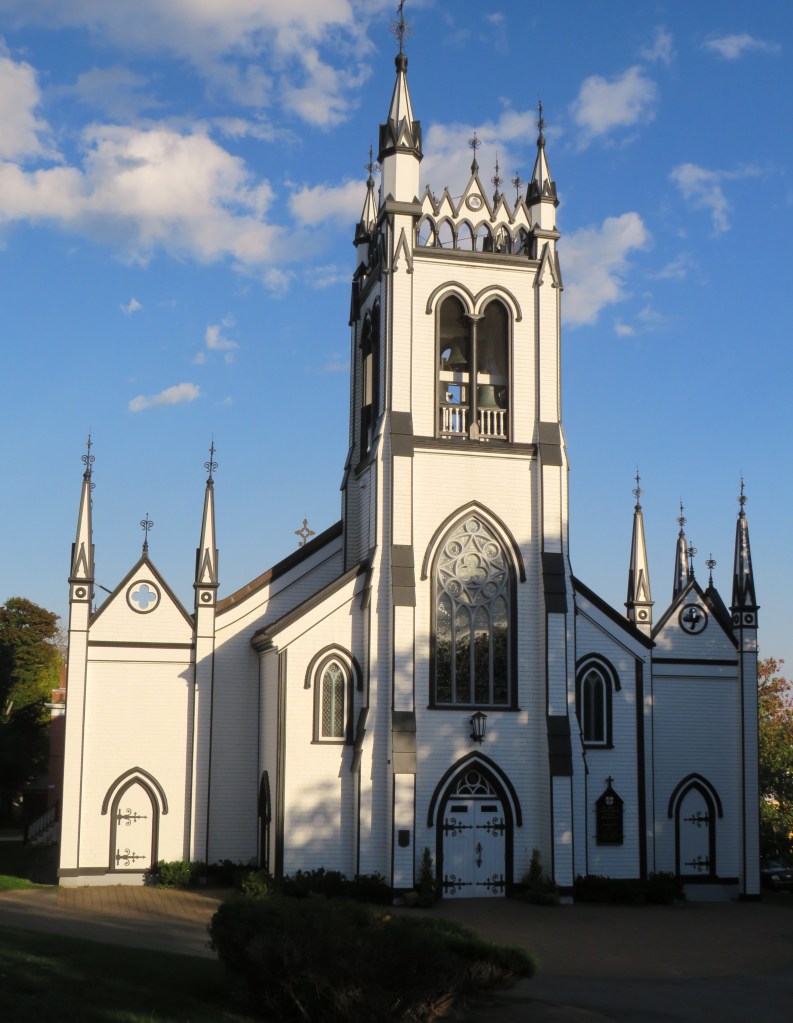 Historic church building with ornate architecture, featuring pointed towers and large stained glass windows, set against a clear blue sky.